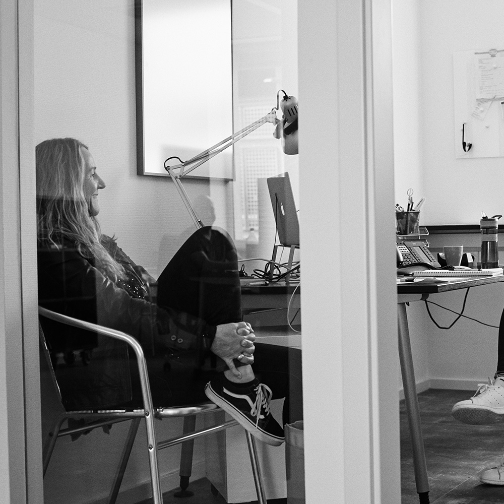 Man sieht zwei Mitarbeiterinnen von FederhenSchneider, die in einem Büro am Schreibtisch sitzen und sich unterhalten. Das Bild ist schwarz/weiß.