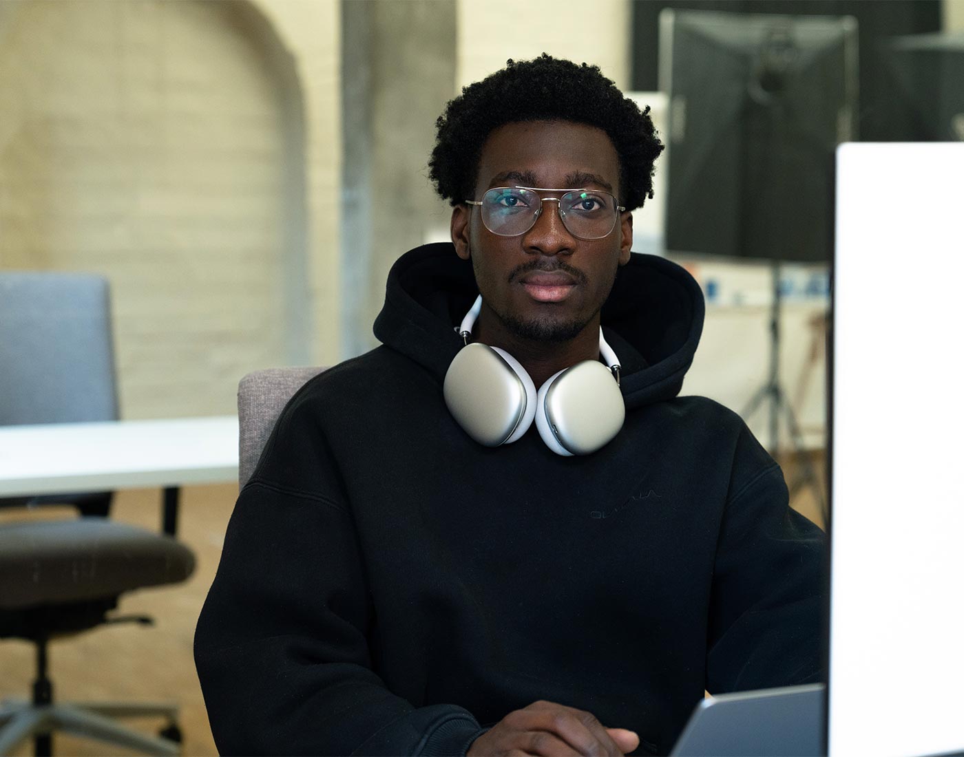 Unser Content Creative Julien sitzt mit Kopfhörern um den Hals an seinem Laptop und schaut in die Kamera.