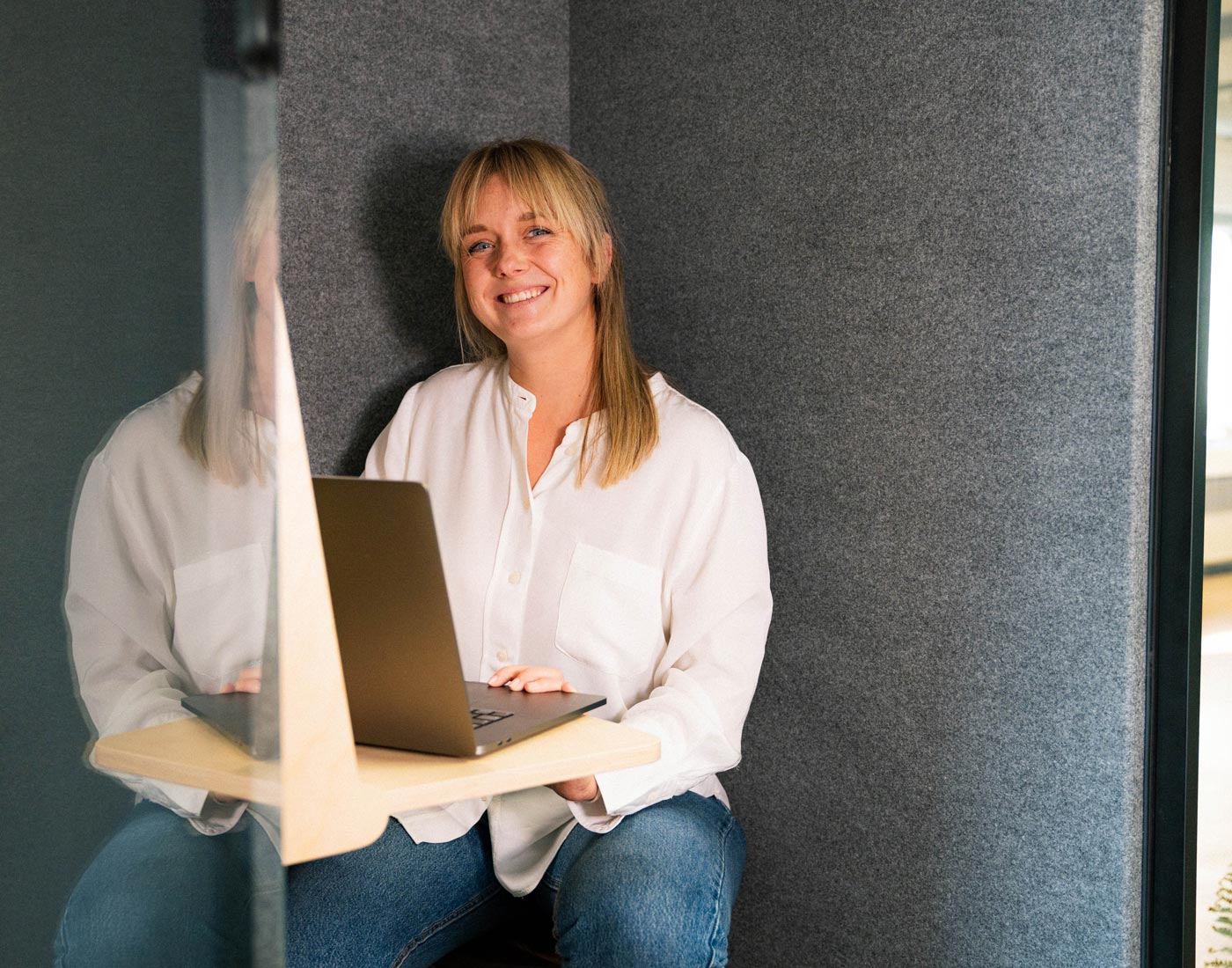 Dieses Bild zeigt eine FederhenSchneider Mitarbeiterin Ende 20 mit langen, hellen Haaren, die an ihrem Schreibtisch sitzt.