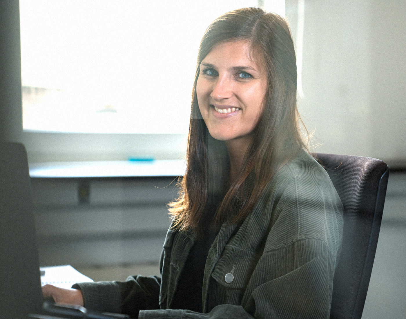 Unsere Projektmanagerin Svenja sitzt an ihrem Schreibtisch und lächelt freundlich in die Kamera.