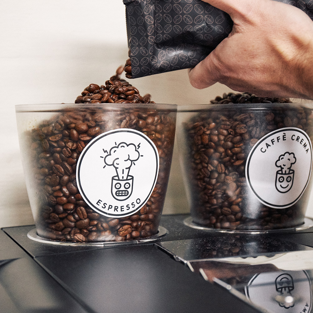 Das Bild zeigt eine Hand, die Kaffeebohnen in den Plexiglasbehälter eines Kaffeevollautomaten schüttet.