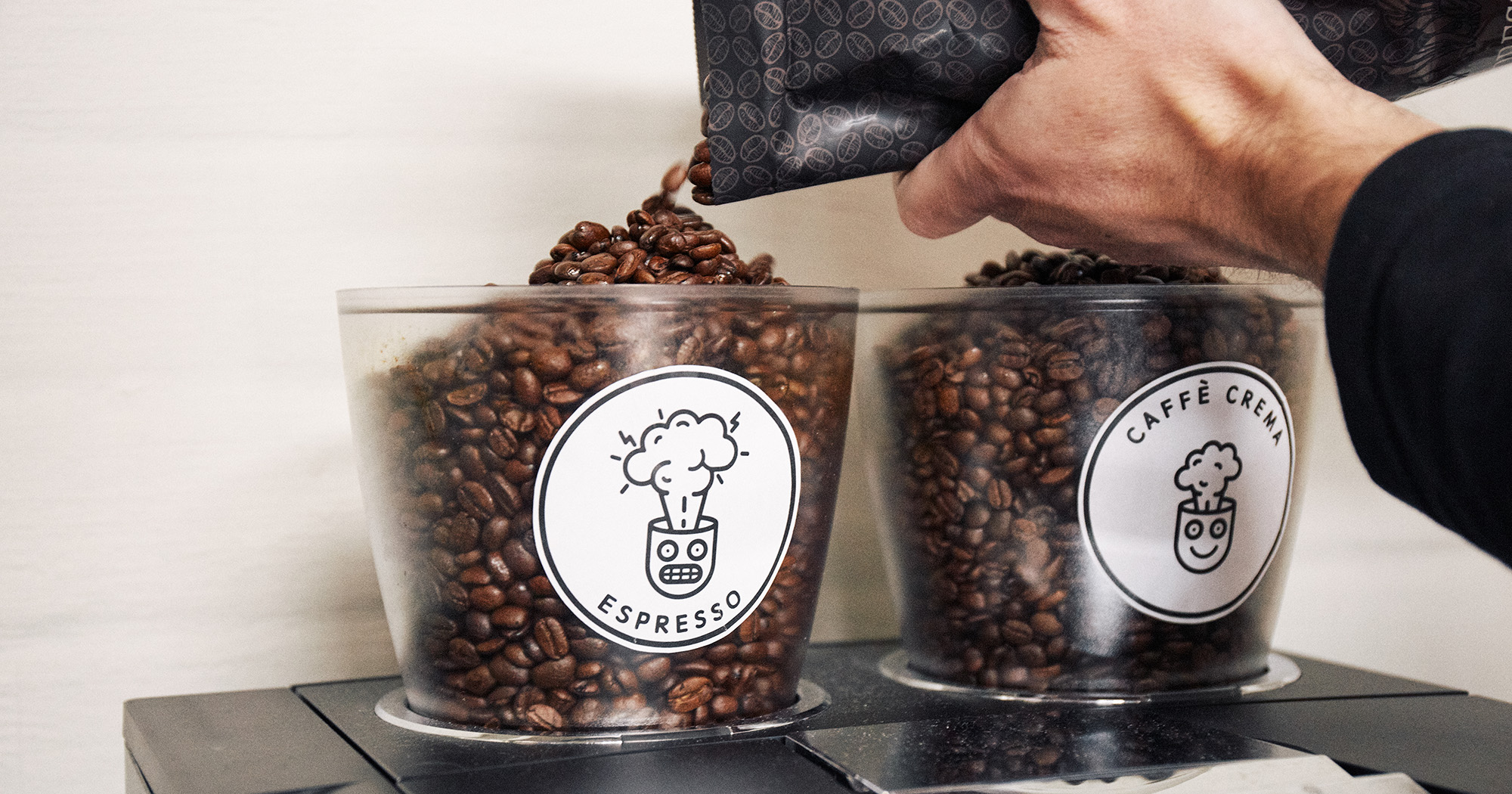 Das Bild zeigt eine Hand, die Kaffeebohnen in den Plexiglasbehälter eines Kaffeevollautomaten schüttet.