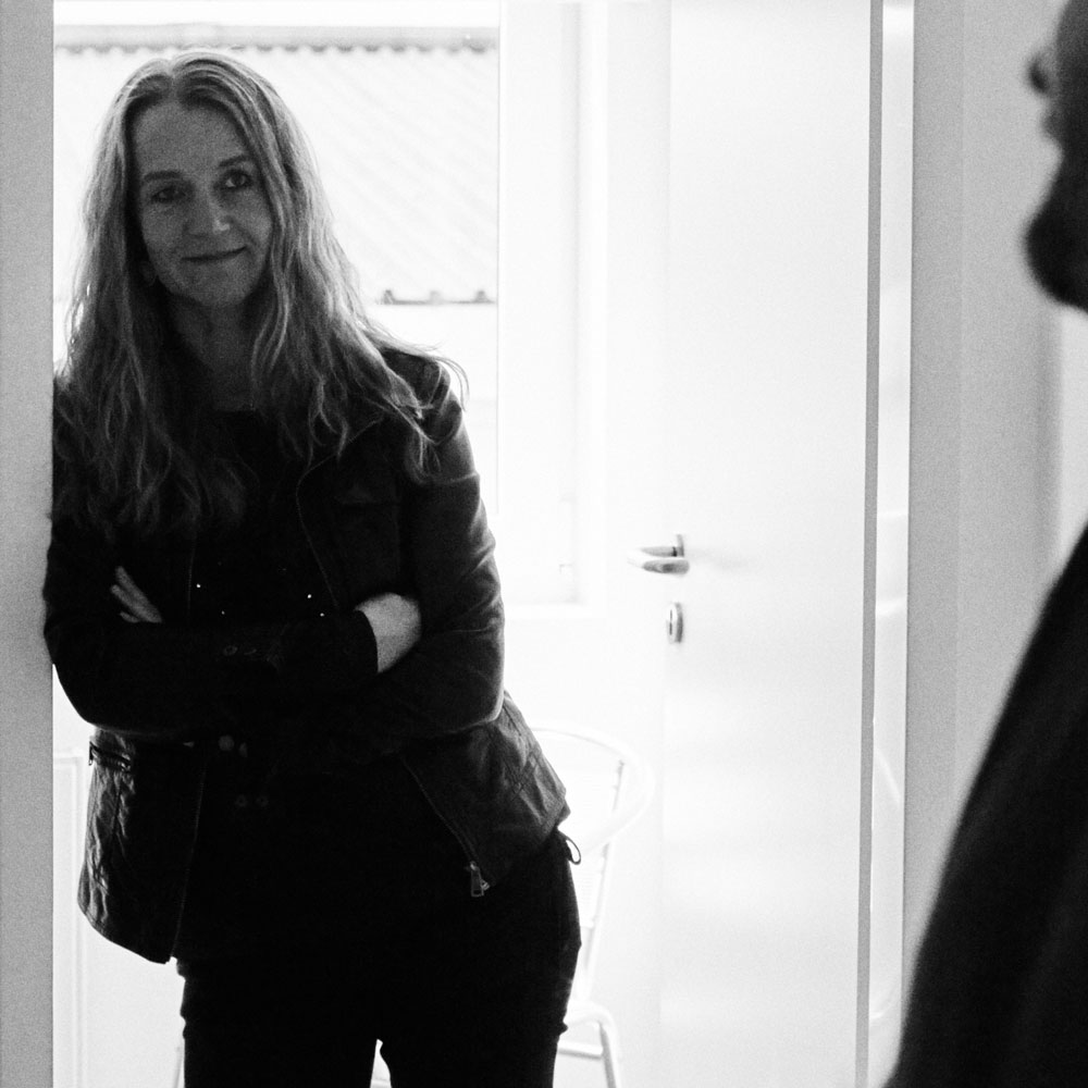 Das Bild zeigt eine FederhenSchneider Mitarbeiterin, die lässig in einem Türrahmen lehnt mit verschränkten Armen.