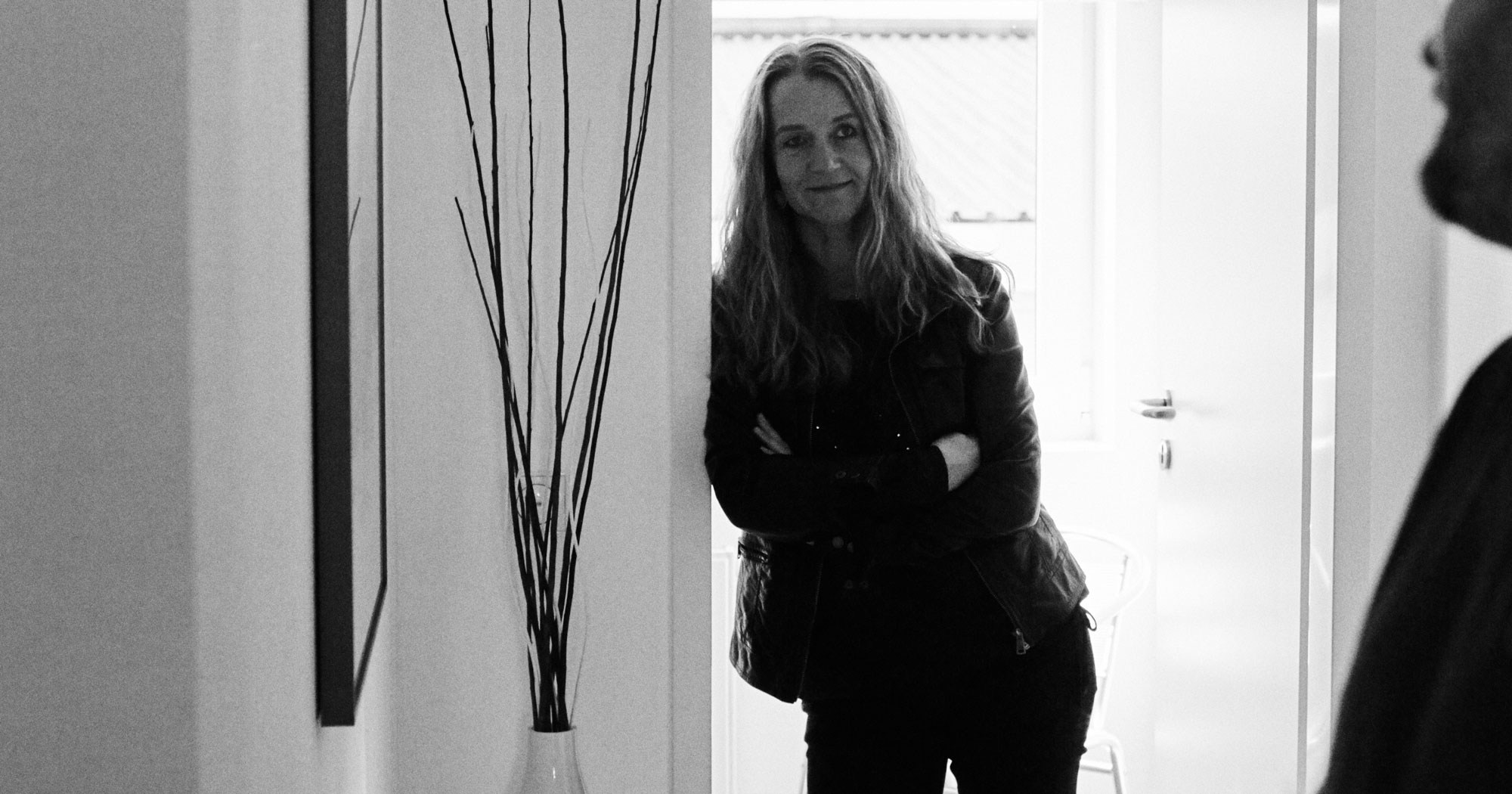 Das Bild zeigt eine FederhenSchneider Mitarbeiterin, die lässig in einem Türrahmen lehnt mit verschränkten Armen.