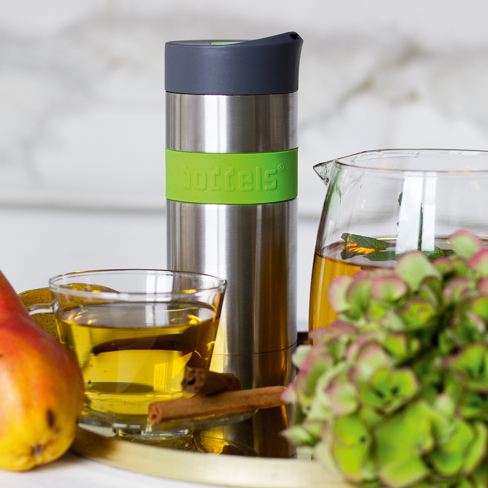 Das Foto zeigt eine Boddels Trinkflasche in grün nebst Teetasse, Birne und Zimtstange auf einem Tablett.