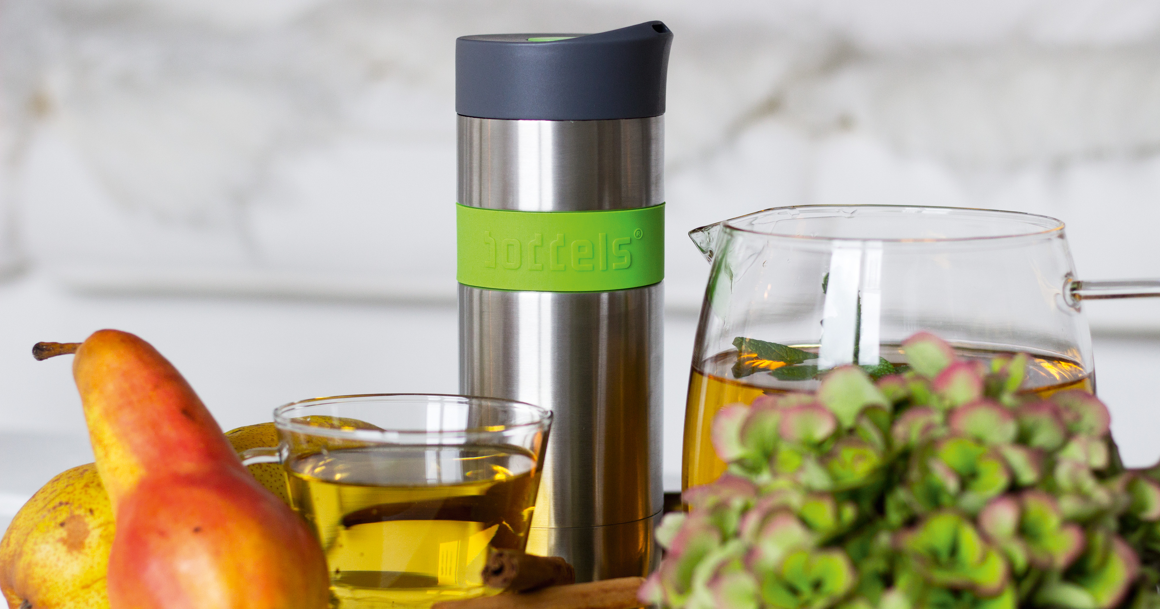 Das Foto zeigt eine Boddels Trinkflasche in grün nebst Teetasse, Birne und Zimtstange auf einem Tablett.