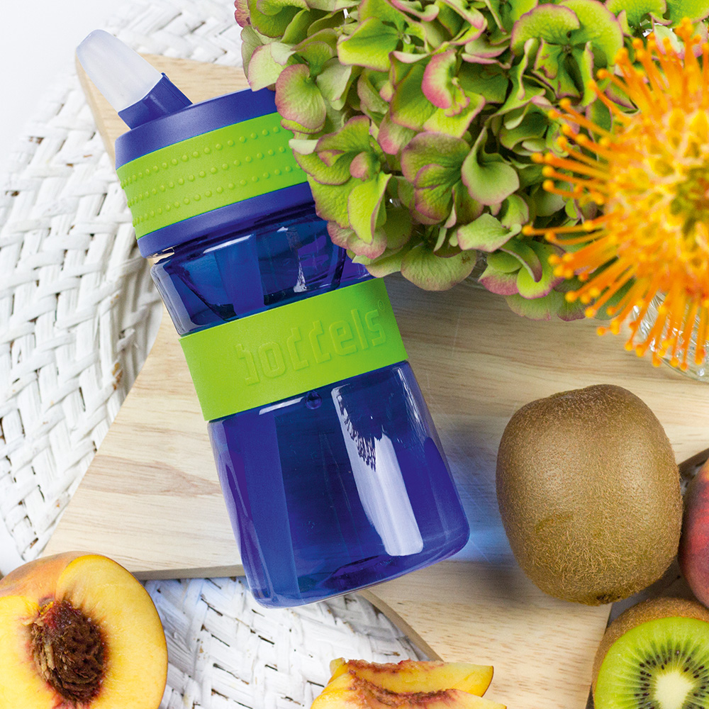 Das Foto zeigt eine Boddels Trinkflasche in grün nebst diversem Obst auf einer weißen Rattan-Oberfläche liegend.