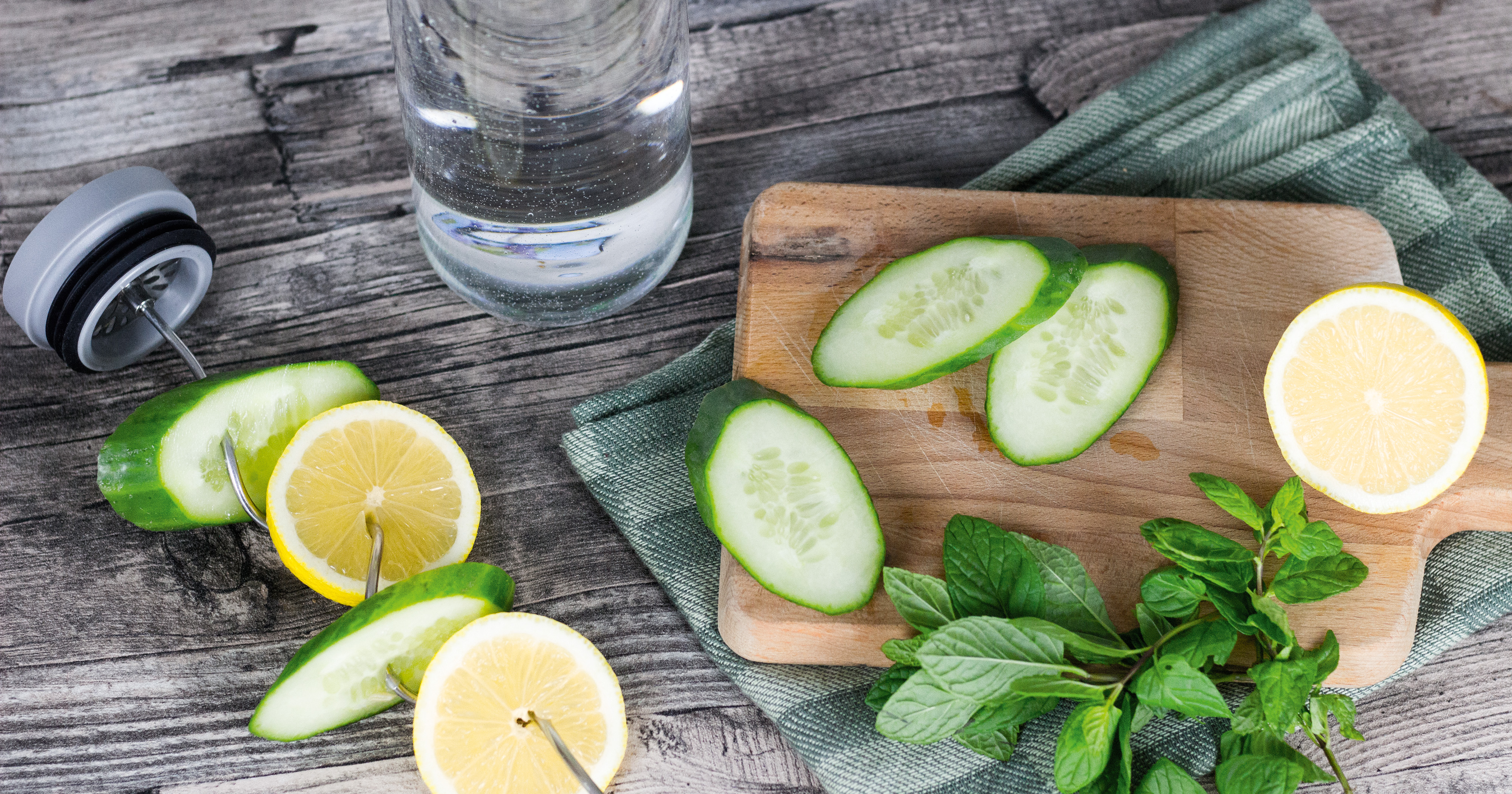 Das Foto zeigt eine Boddels Glaskaraffe in grün mit danebenliegendem Fruchtspieß gespickt mit Scheiben von Zitrone und Gurke im Wechsel.