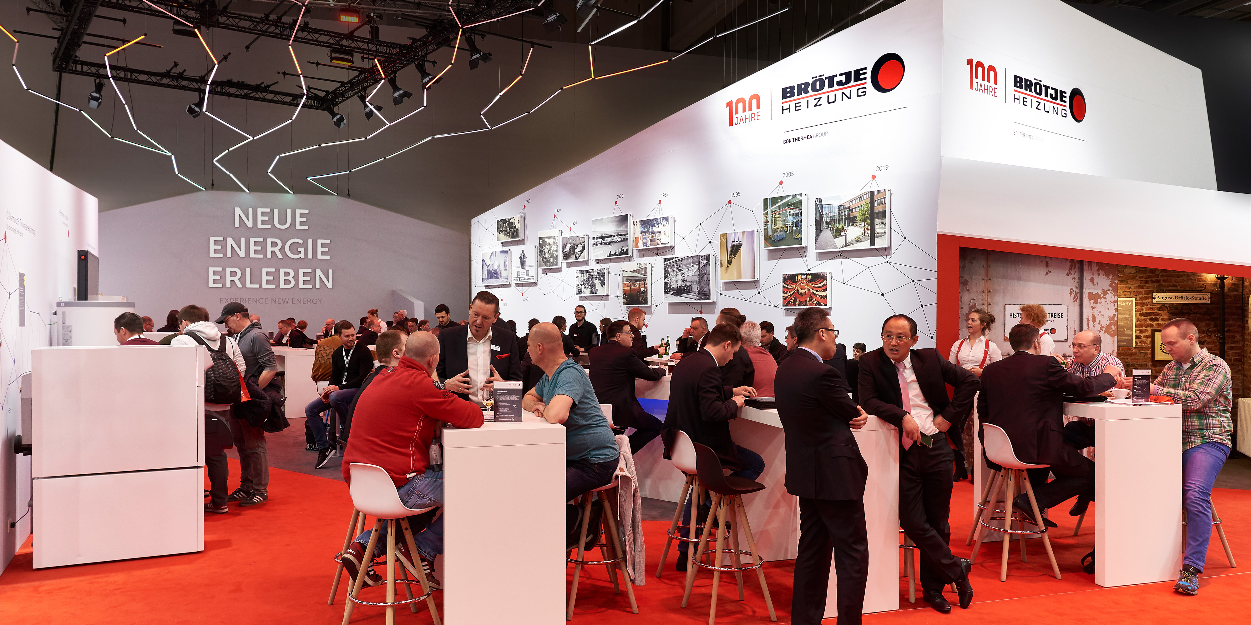 Das Foto zeigt den Catering-Bereich des Messestands von BRÖTJE mit Blick auf den Messeclaim „Neue Energie erleben“. Der Stand ist sehr belebt, Menschen unterhalten sich oder erkunden die Ausstellungsstücke.