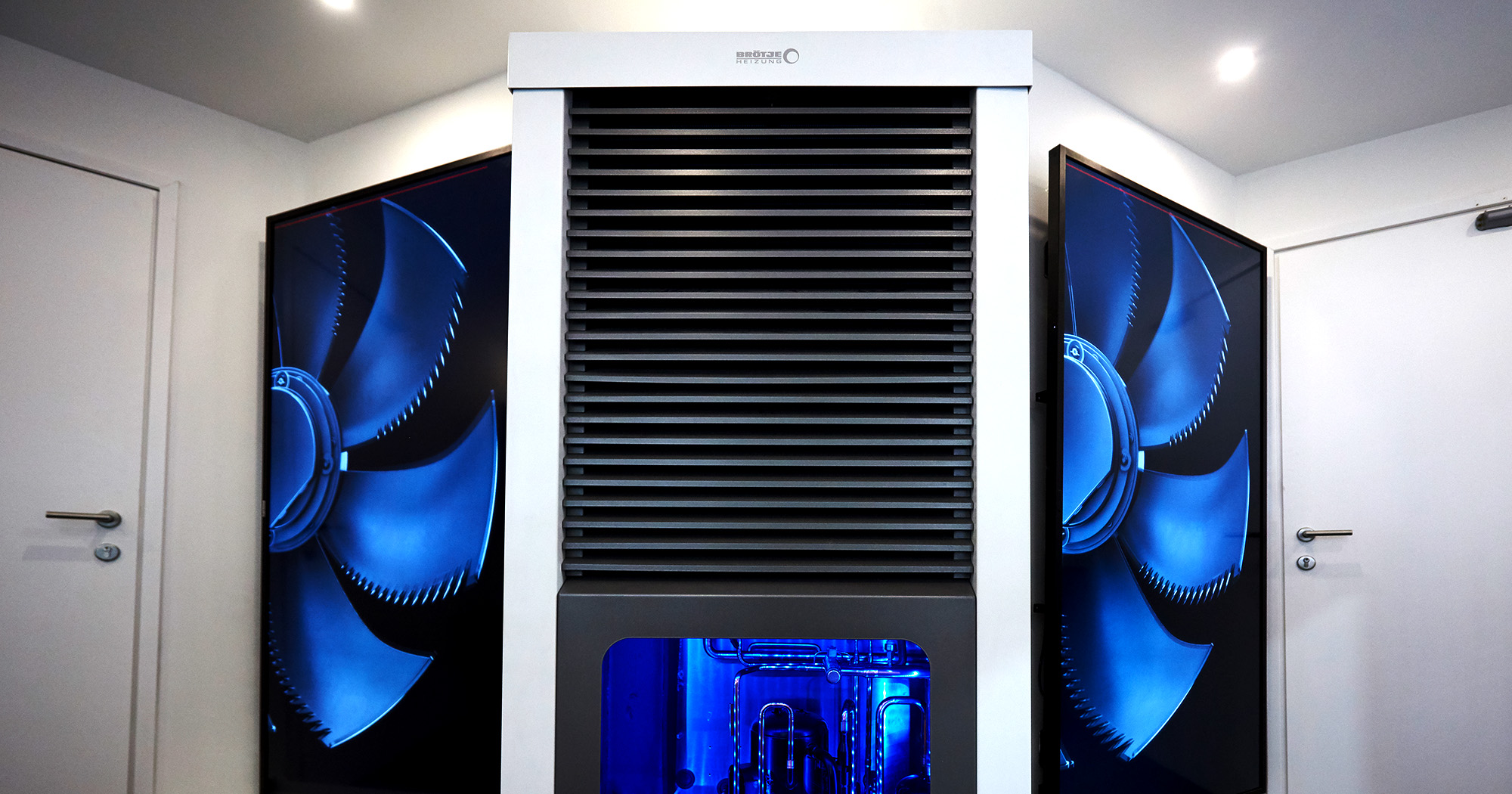 Das Foto zeigt eine BRÖTJE Wärmepumpe, daneben große Screens, die den „Eulenflügel“ der BRÖTJE BLW Neo zeigen.