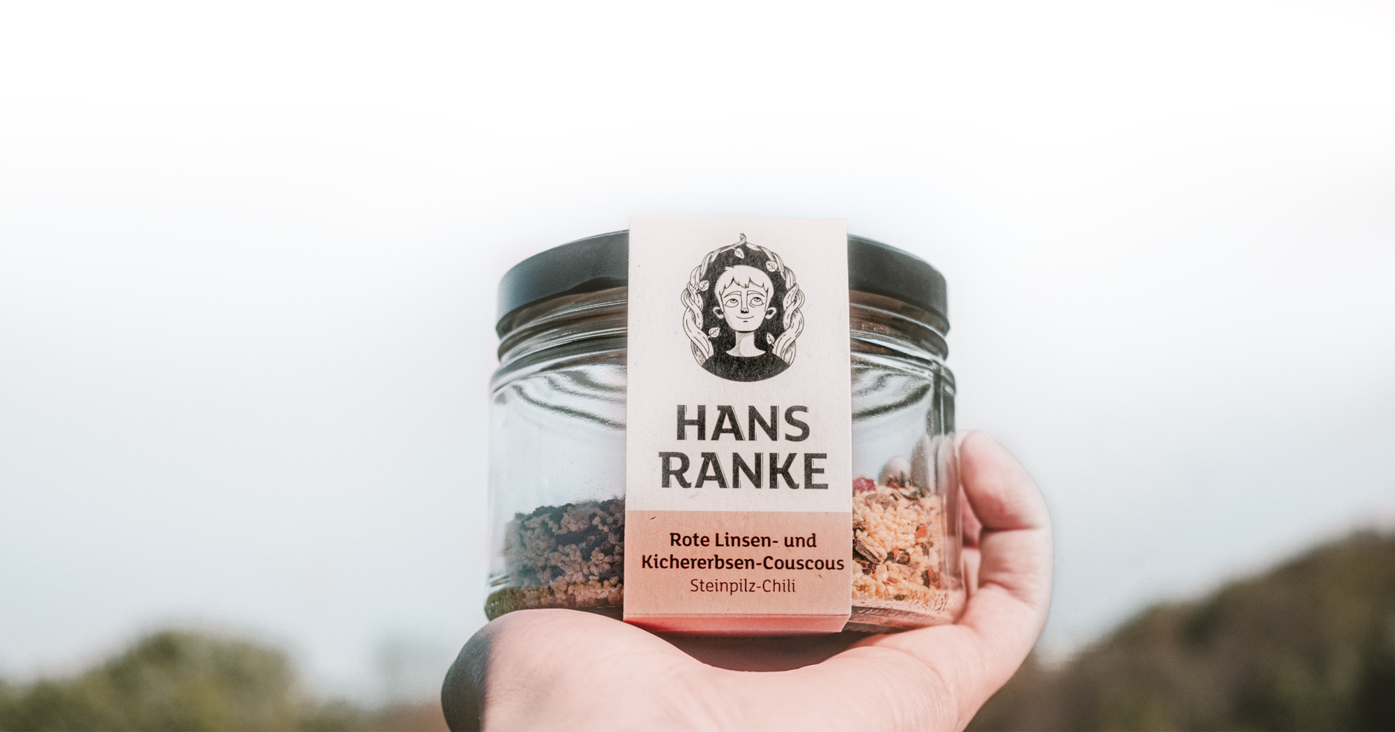Ein Glas Hans Ranke Couscous von einer Hand gegen den Himmel gehalten