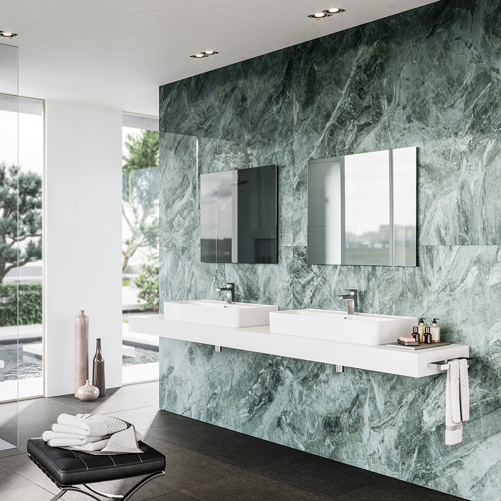 Das Bild zeigt ein modernes, helles Badezimmer als 3D Rendering. Im Hintergrund eine Glasfront, im Vordergrund ein schwebendes Doppelwaschbecken vor dunkelgrünen Marmorfließen, nebst schwarzem Lederhocker, auf dem ein Handtuch liegt.