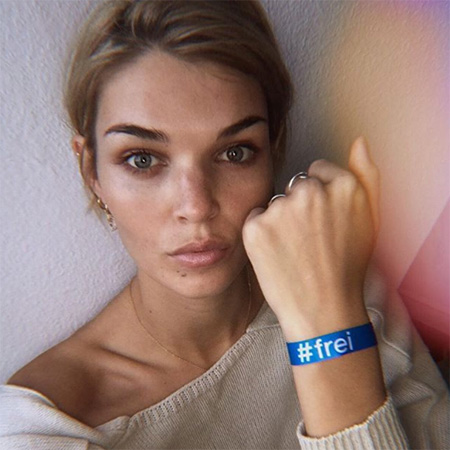 Das Foto zeigt den Oberkörper einer blonden Frau mit Zopf, die ihren Arm mit blauem #frei Band in die Kamera hält.