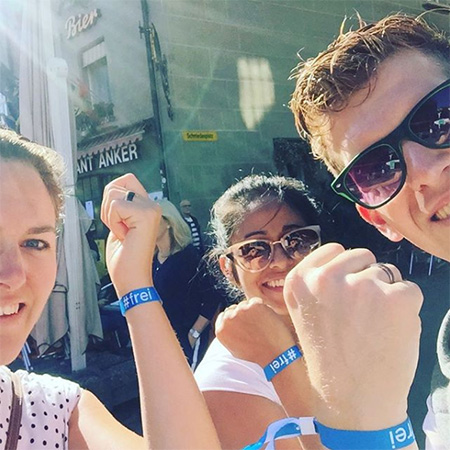 Das Foto zeigt ein Selfi mit drei Menschen vor einer Glasfassade. Sie strecken ihren Arm mit dem blauen #frei Band in die Kamera.