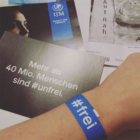 Das Foto zeigt einen Arm mit dem blauen #frei Band, der in die Kamera ragt.  Im Hintergrund eine Karte, auf der steht „Mehr als 40 Mio. Menschen sind #unfrei“.