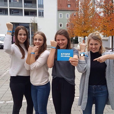 Das Foto zeigt vier junge Frauen. Sie strecken ihren Arm mit dem blauen #frei Band in die Kamera. Eine hält zusätzlich eine Karte, auf der steht „Stoppt Sklaverei“.