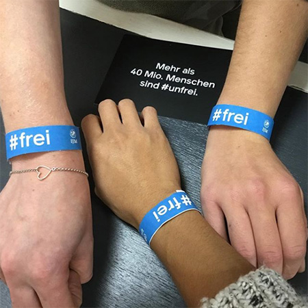 Das Foto zeigt drei Arme mit dem blauen #frei Bändern, die aus verschiedenen Richtungen in die Kamera ragen. Im Hintergrund eine Karte, auf der steht „Mehr als 40 Mio. Menschen sind #unfrei“.