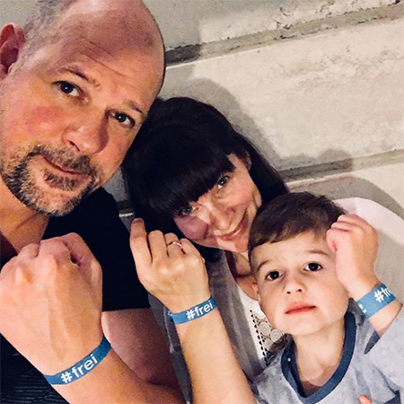 Das Foto zeigt eine Familie. Mutter, Vater und Sohn tragen ein blaues #frei Band. Im Hintergrund einem Betonwand.