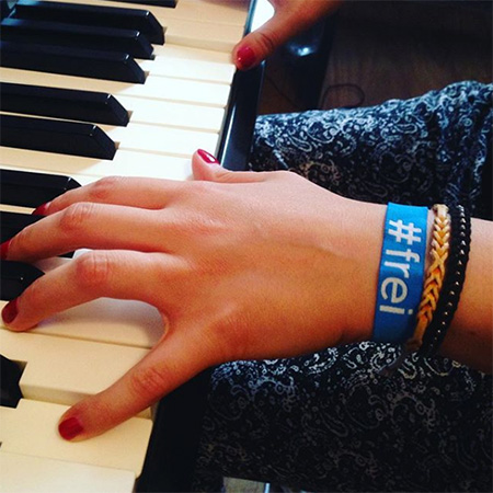 Das Foto zeigt eine Hand mit blauem #frei Band, die ins Bild ragt und Klavier spielt.