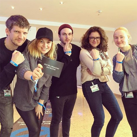 Das Foto zeigt vier junge Menschen. Sie strecken ihren Arm mit dem blauen #frei Band in die Kamera. Eine hält zusätzlich eine Karte, auf der steht „Mehr als 40 Mio. Menschen sind #unfrei“.