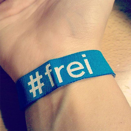 Das Foto zeigt einen ausgestreckten Arm mit #frei Bändchen aus der Nähe.