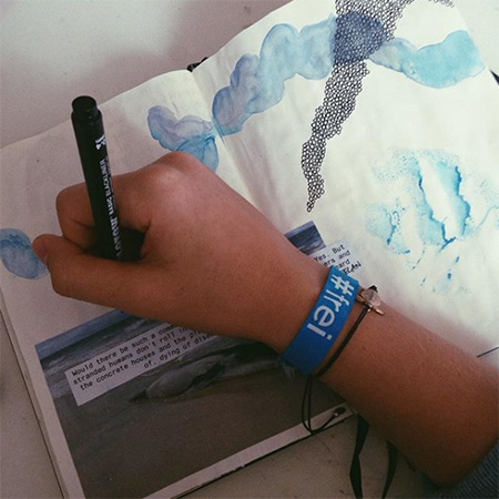 Das Foto zeigt einen ausgestreckten Arm mit #frei Bändchen, der einen Filzstift hält. Darunter ein Malbuch.