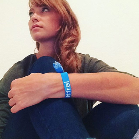 Das Foto zeigt eine Frau, die ihre Knie umarmt mit blauem #frei Band am Handgelenk.