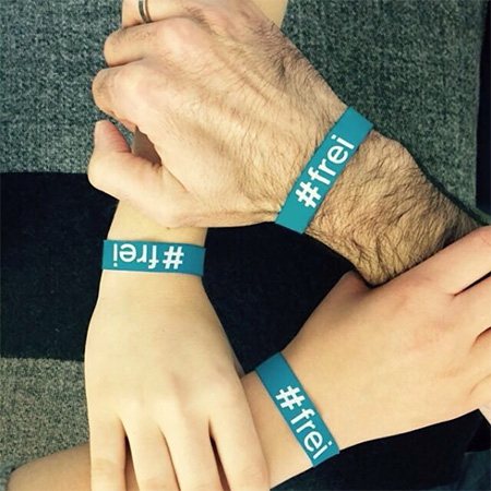 Das Foto zeigt drei Arme mit #frei Band am Handgelenk. Mit den Händen umfassen sie das Handgelenk des benachbarten Arms und bilden so ein Dreieck.