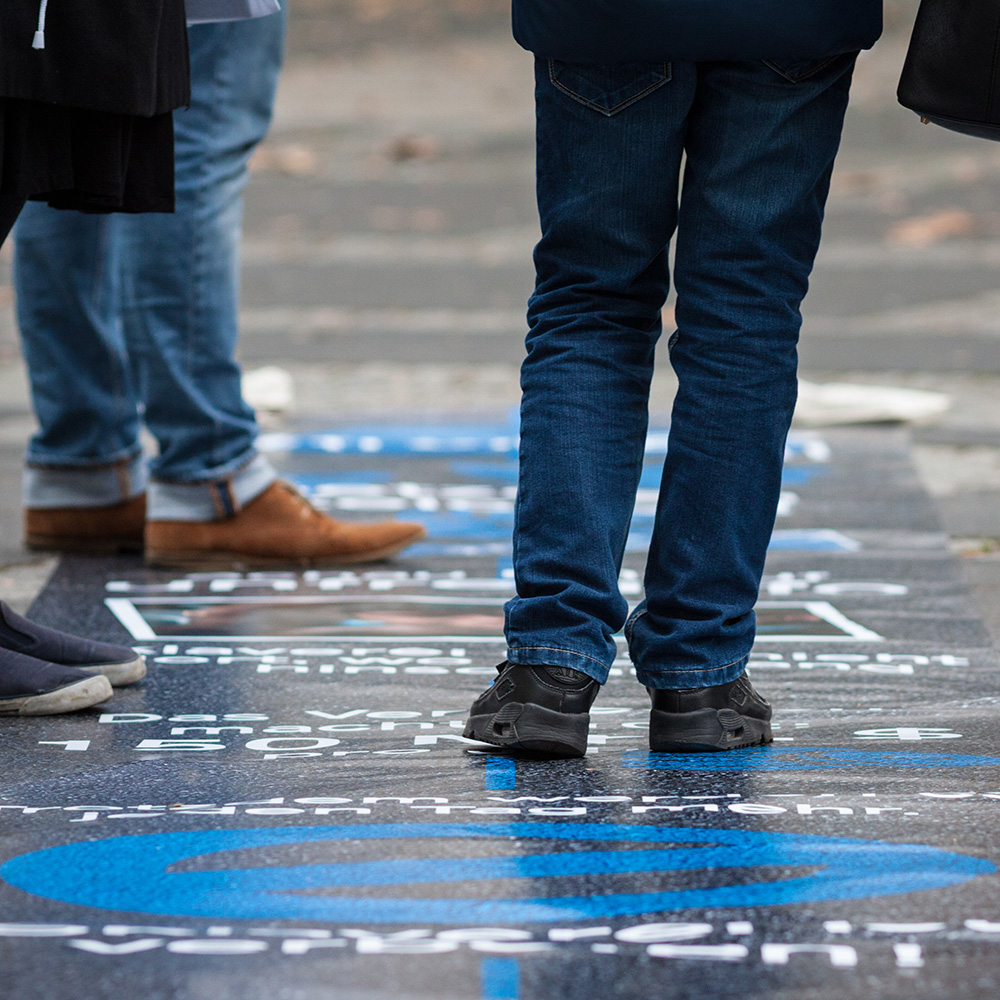 Das Bild zeigt den Boden einer Straße mit blauer Malerei und mehreren Beinen, die auf der Malerei stehen.
