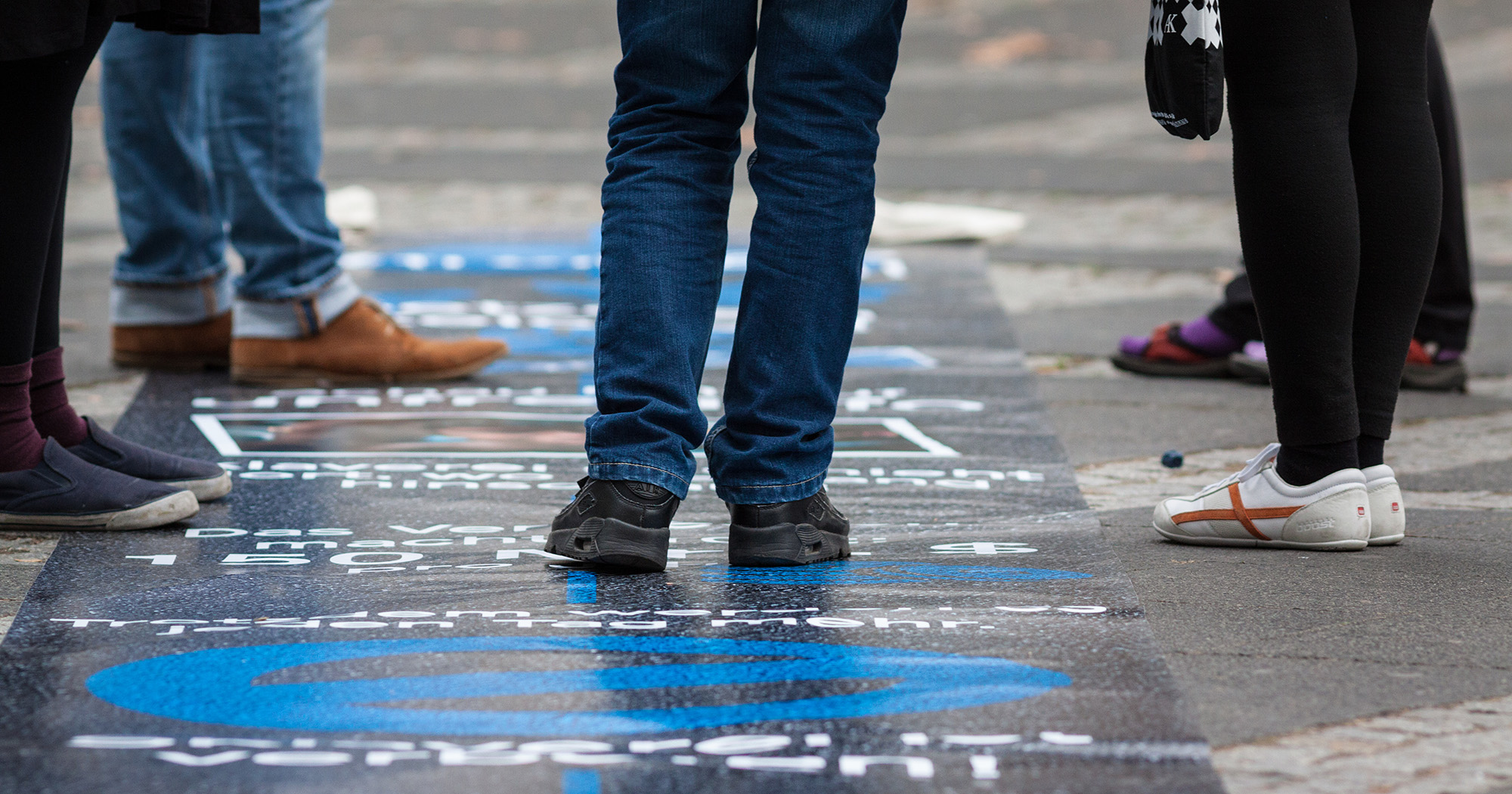 Das Bild zeigt den Boden einer Straße mit blauer Malerei und mehreren Beinen, die auf der Malerei stehen.