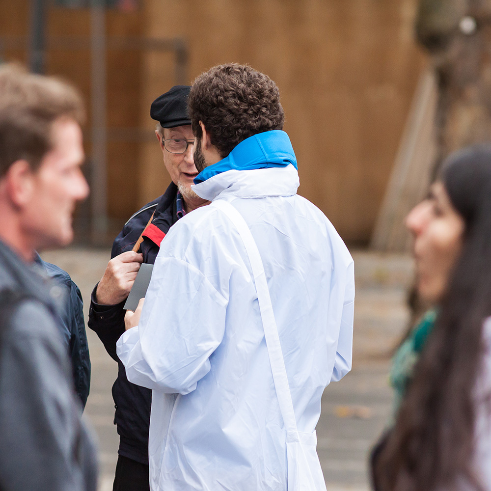 Das Bild zeigt einen Mann auf der Straße von hinten. Er redet mit einem anderen Mann.