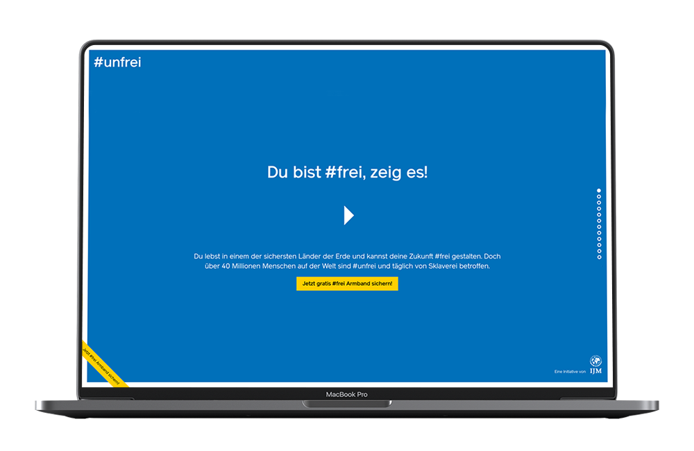 Man sieht einen Laptop, darauf ist die Startseite der unfrei Website zu sehen mit Schrift auf weißem Grund und einem Play-Button.