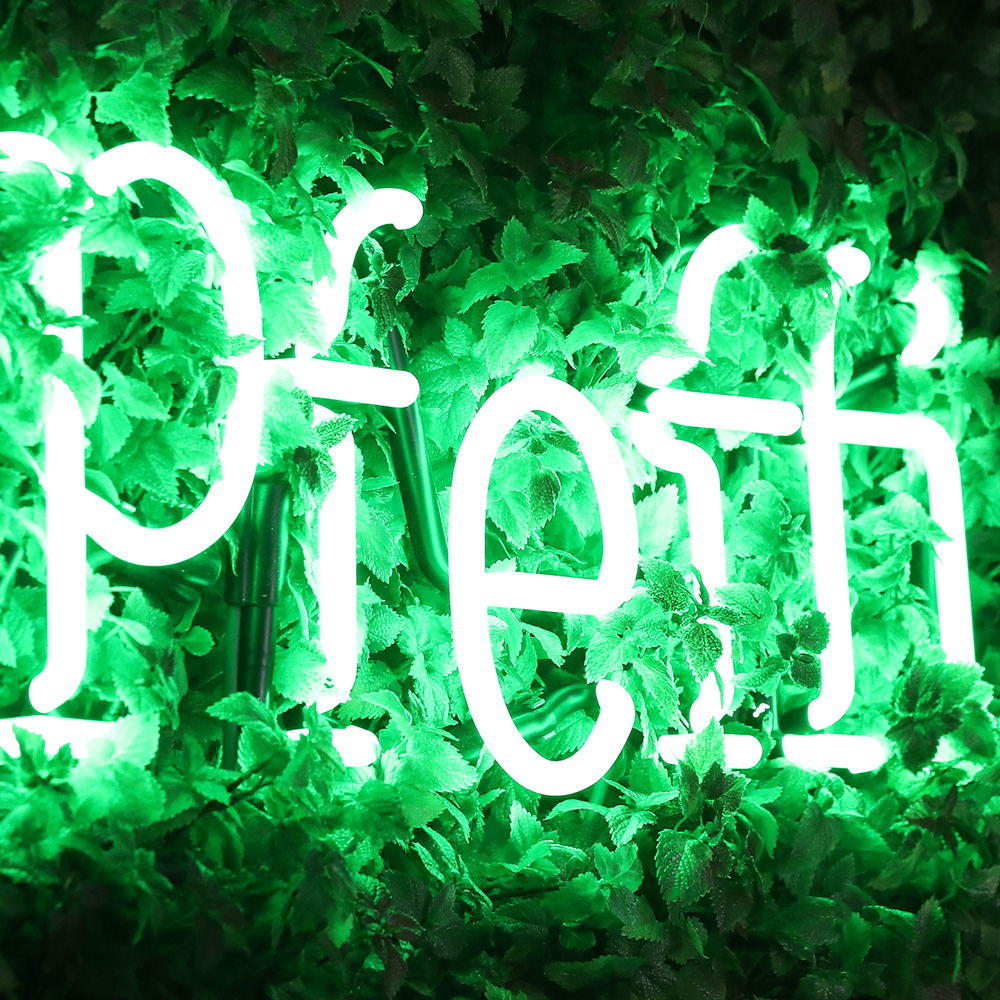 Das Foto zeigt eine grün bepflanzte Wand mit „#pfeffi“ Leuchtschrift.