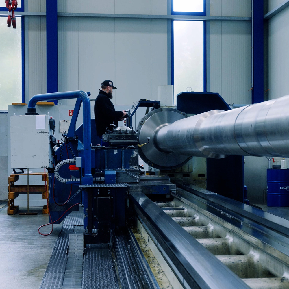 Industriemaschine in einer Fertigungshalle der Rolf Kind GmbH – Mitarbeiter bearbeitet ein langes Werkstück