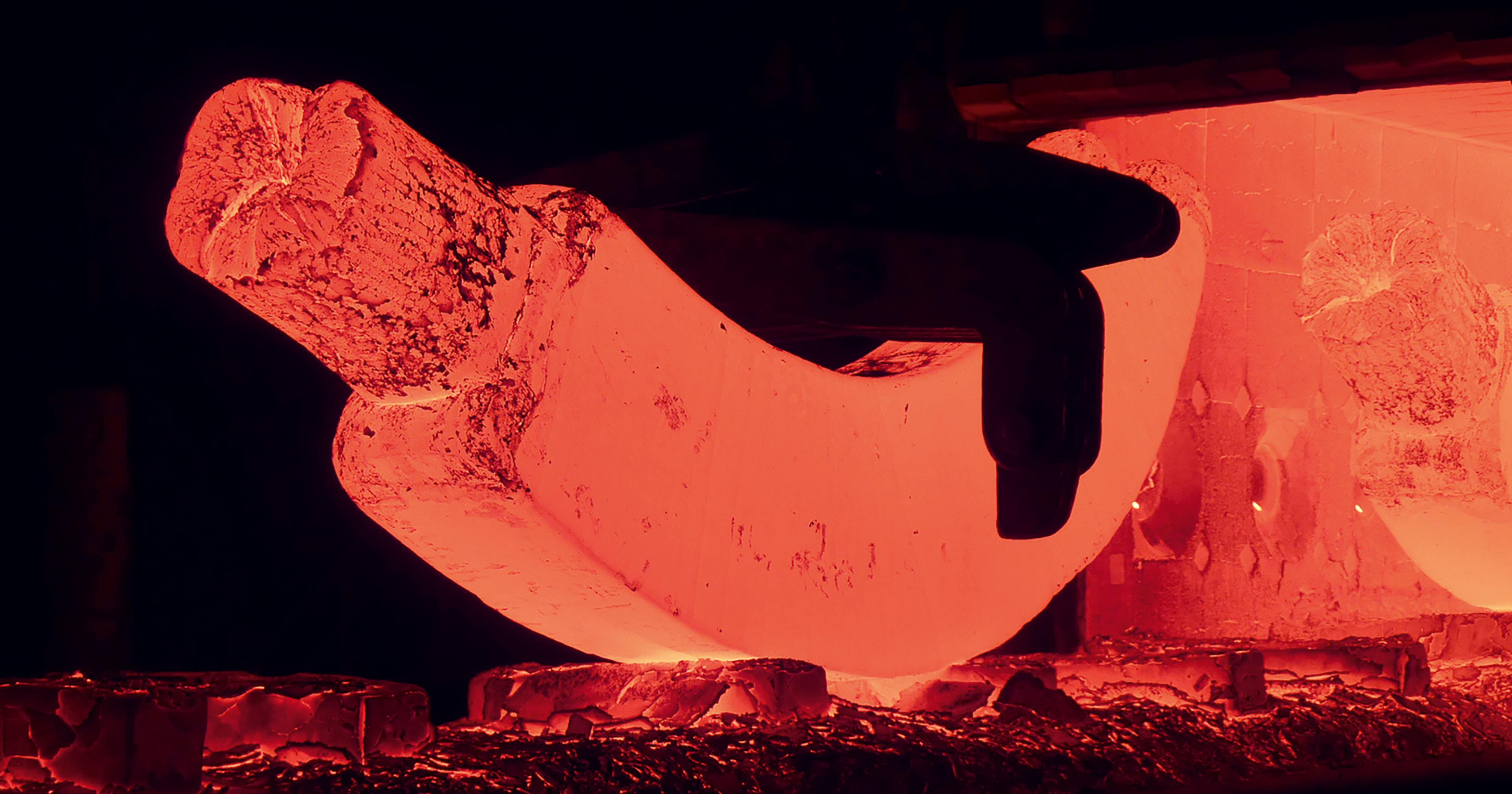 Man sieht ein Stück glühendes, gebogenes Metall.