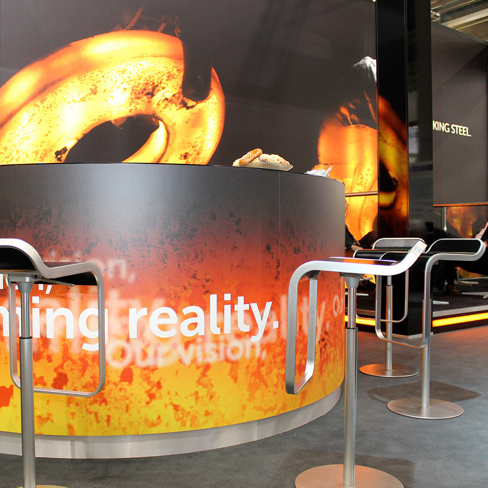 Das Foto zeigt einen runden Hochtisch mit Barhockern und RKind-Branding auf einer Messe.