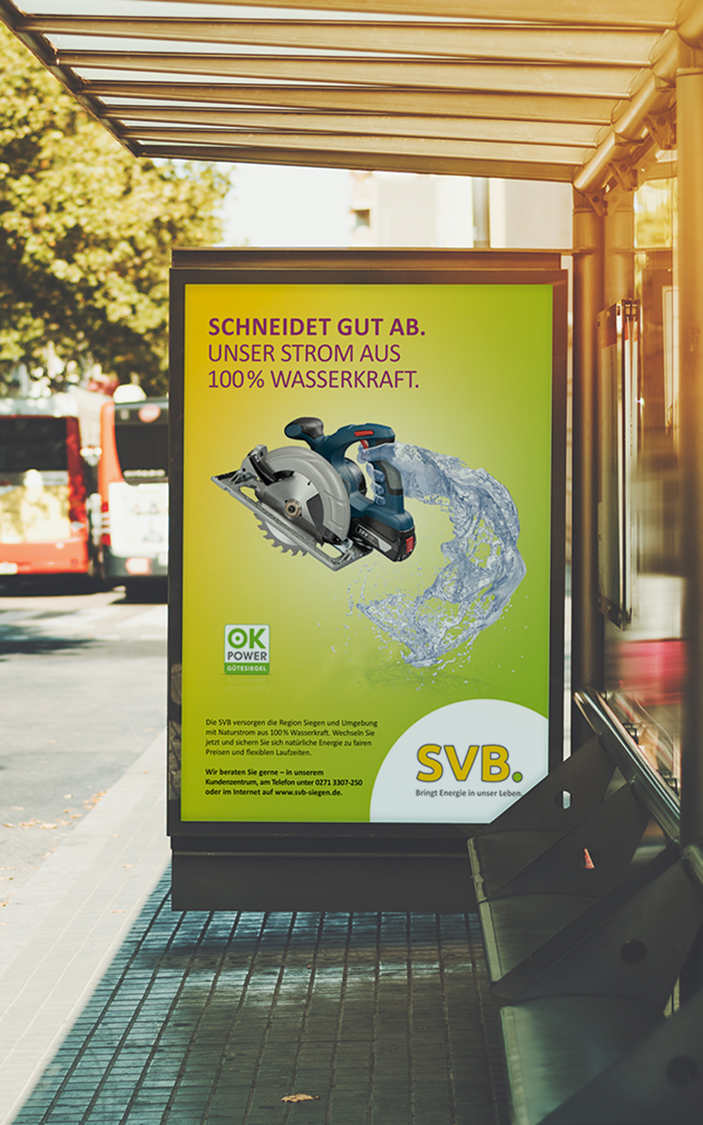 Das Foto zeigt ein Citylight an einer Bushaltestelle. Man sieht ein Poster auf dem eine Hand aus Wasser eine elektrische Säge hält. Darüber die Headline „Schneidet gut ab. Unser Strom aus 100% Wasserkraft.“ auf gelb/grünem Grund.