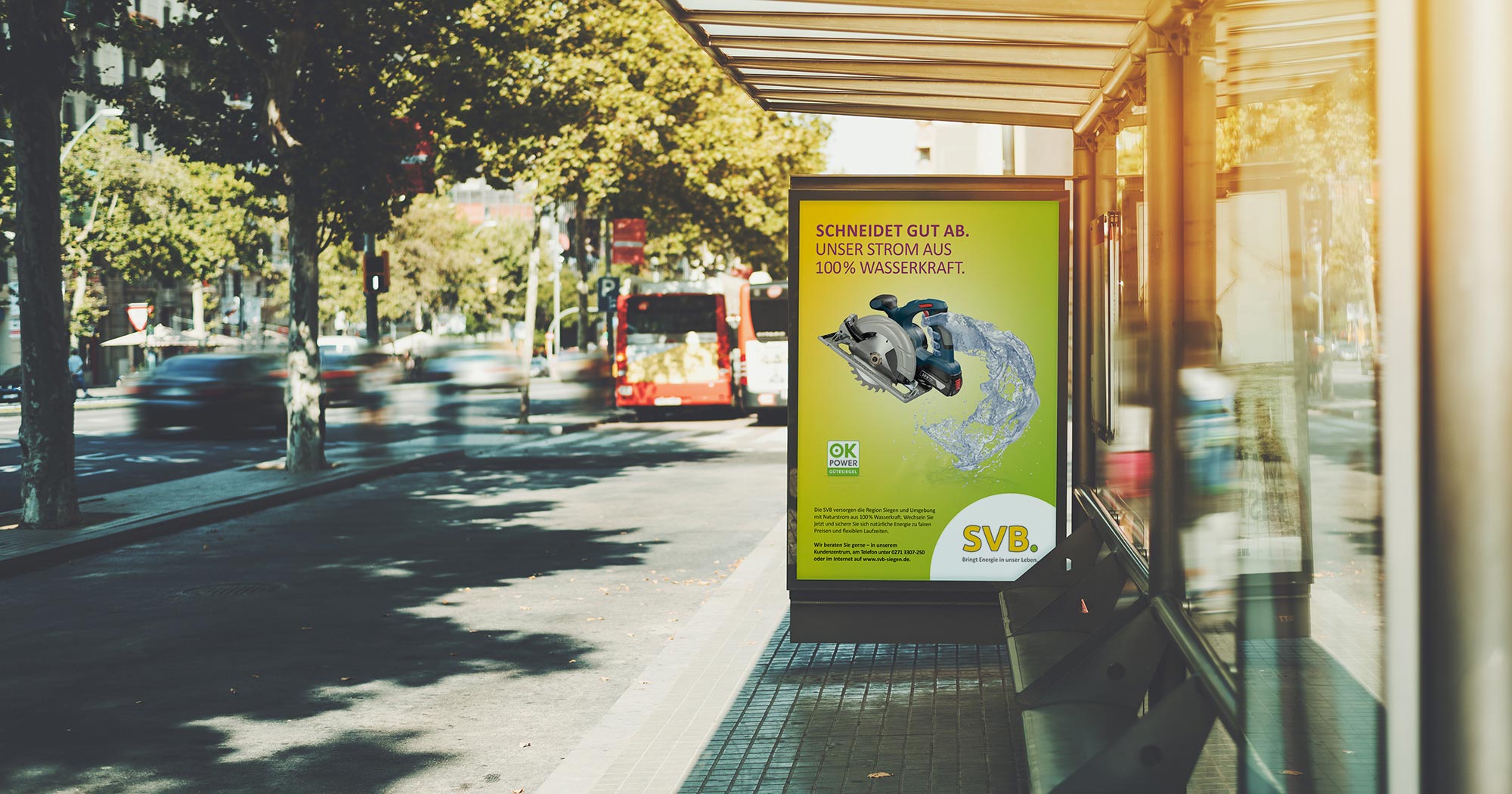 Das Foto zeigt ein Citylight an einer Bushaltestelle. Man sieht ein Poster auf dem eine Hand aus Wasser eine elektrische Säge hält. Darüber die Headline „Schneidet gut ab. Unser Strom aus 100% Wasserkraft.“ auf gelb/grünem Grund.